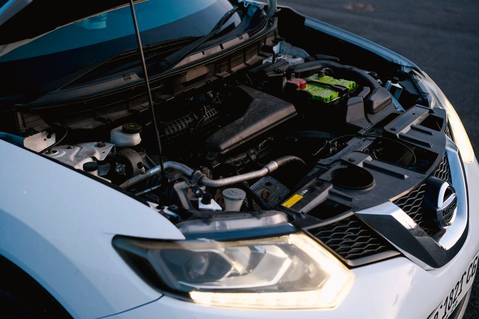 Close-up of a car engine with hood open, showcasing various mechanical components and details.